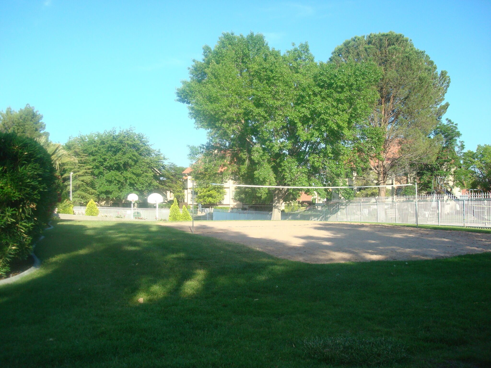 Un parque con cancha de baloncesto, árboles y una valla.