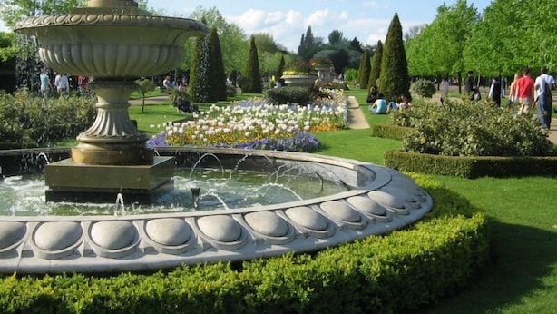 Um jardim formal com uma fonte central, gramados bem cuidados e sebes podadas.