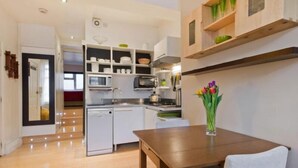 Cozinha moderna com armários brancos, micro-ondas, torradeira e pia. Há uma mesa de madeira com um vaso de flores.