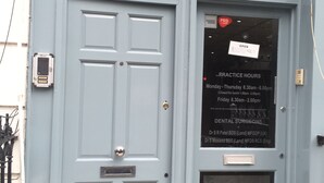Uma porta azul clara com uma placa indicando 'OPEN ESTHETIQUE' e 'PRACTICE HOURS' para cirurgiões dentistas.