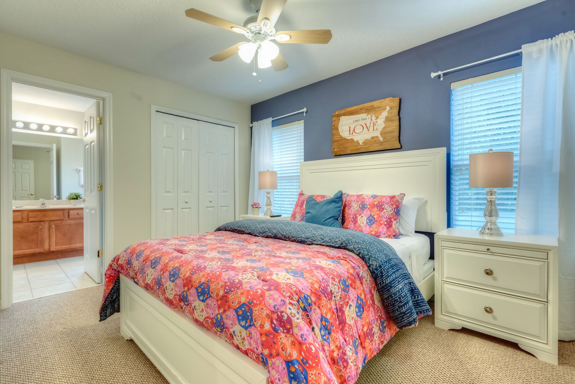A bedroom with a bed, a nightstand, a ceiling fan, a wall map, and a bathroom visible through an open door.
