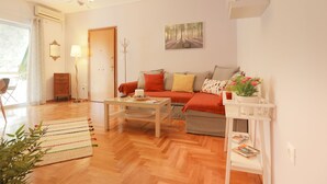 A living room with a sofa, coffee table, and a white side table with a plant. - Cosy & Bright 2 Bedroom Apartment in Koukaki (Athens)