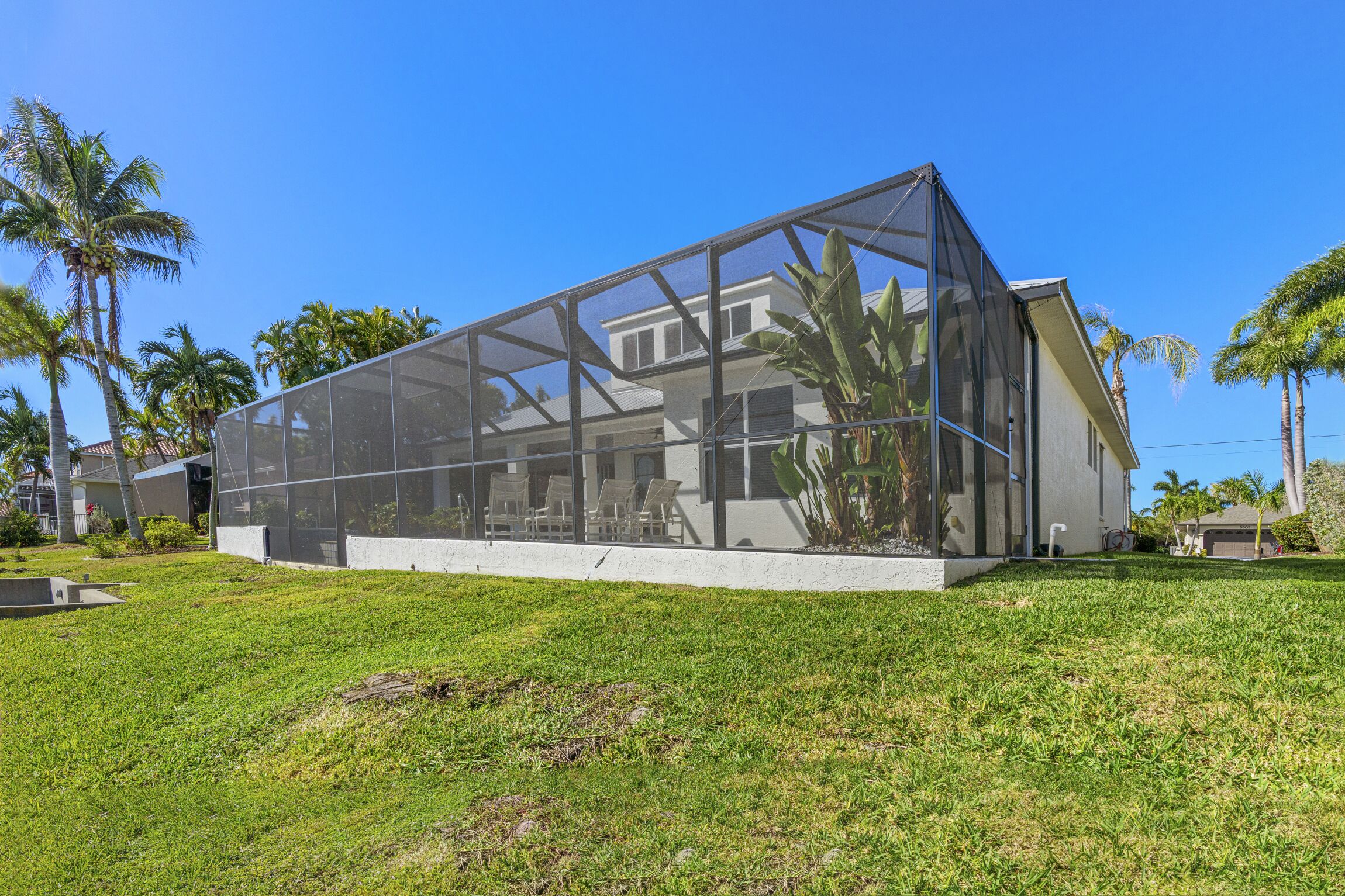 A modern house with a large glass enclosure, surrounded by a well-maintained lawn and palm trees.