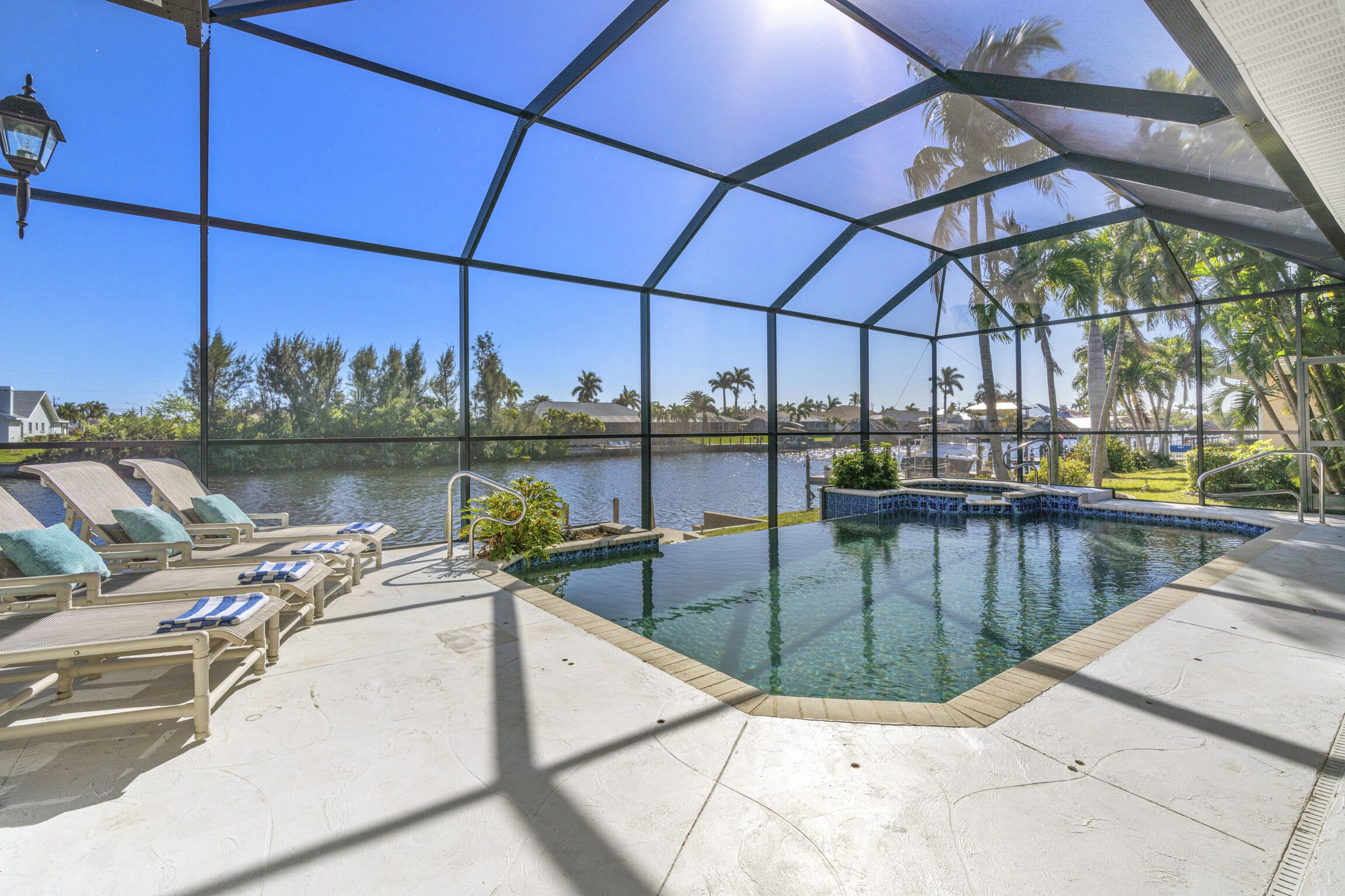 A pool area with lounge chairs and a view of a lake and palm trees.