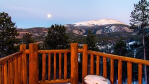 Une terrasse en bois avec un banc, donnant sur une chaîne de montagnes enneigées.