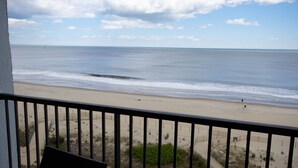 A beach view from a balcony with a railing, sandy beach, and ocean.