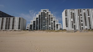 A beachfront hotel with multiple floors, balconies, and a sandy beach in the foreground.