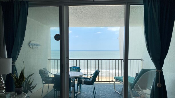 A balcony with a table and chairs, a potted plant, and a view of the ocean.