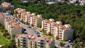 A coastal residential area with multi-story buildings, a beach, and palm trees. - Beachfront Condo+Pool+Backup Power+Full AC+FREEpkg+75TVSURR SYS (loiza)
