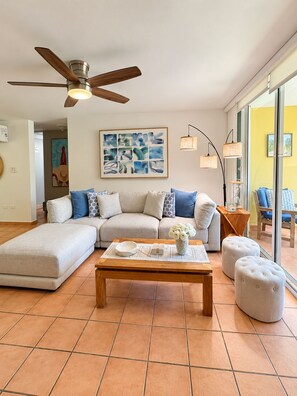 A living room with a sectional sofa, a coffee table, a ceiling fan, and artwork on the wall.