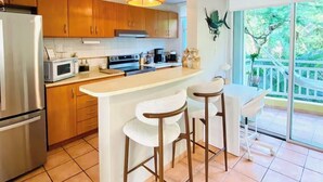 A modern kitchen with wooden cabinets, a stainless steel refrigerator, a microwave, and a large island with bar stools. - Beachfront Condo+Pool+Backup Power+Full AC+FREEpkg+75TVSURR SYS (loiza)