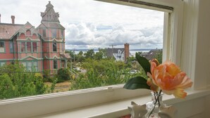 Une vue depuis une fenêtre, avec en arrière-plan un bâtiment de style victorien, un vase avec une fleur et deux statuettes sur une table.