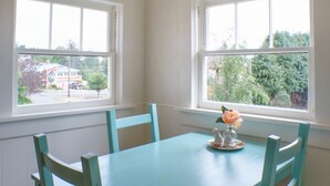 Un coin repas avec une table bleu clair et des chaises assorties, une suspension en forme de lanterne en papier et des fenêtres donnant sur la verdure et les bâtiments environnants.