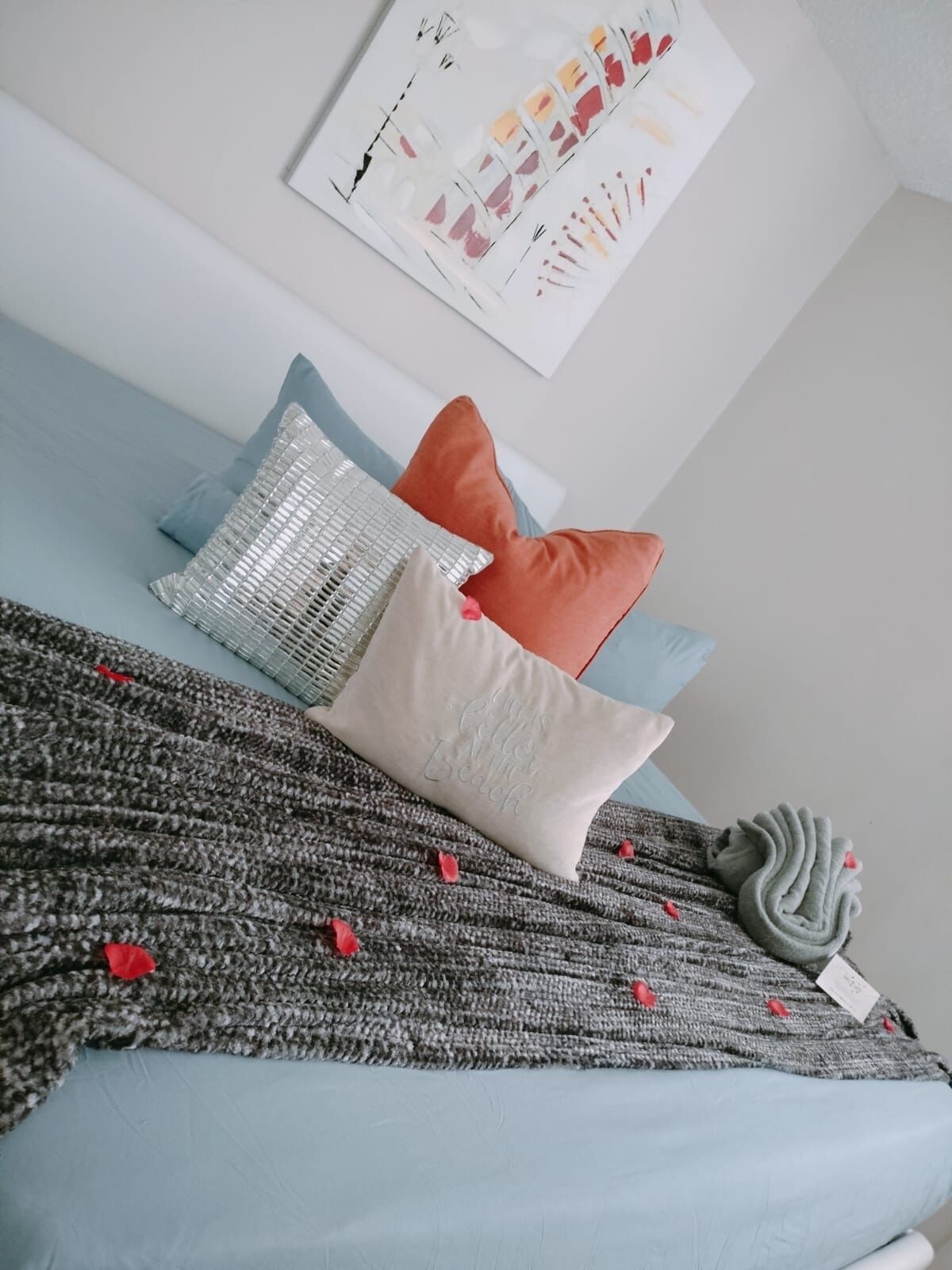 A neatly arranged bed with a grey knitted blanket, two pillows, and a decorative item.