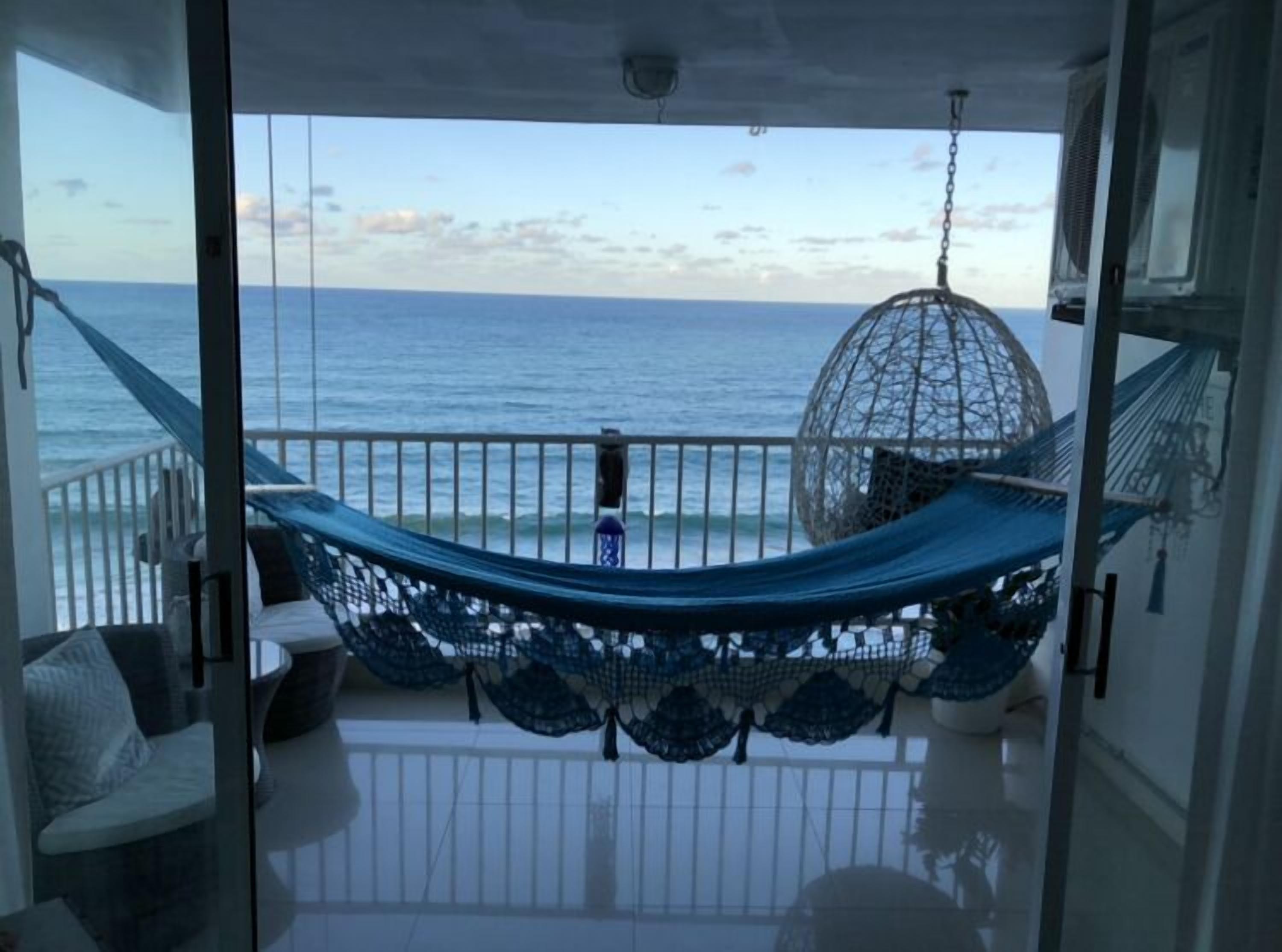 Un balcone con un'amaca, una sedia sospesa e vista sull'oceano.