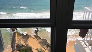A view of the ocean through a window, with waves crashing onto a sandy beach and rocky cliffs. - OCEAN VIEW GORGEOUS 1 BEDROOM CONDO APT A MILLION DOLLAR VIEW.5stars☀️BEST APT (Luquillo)