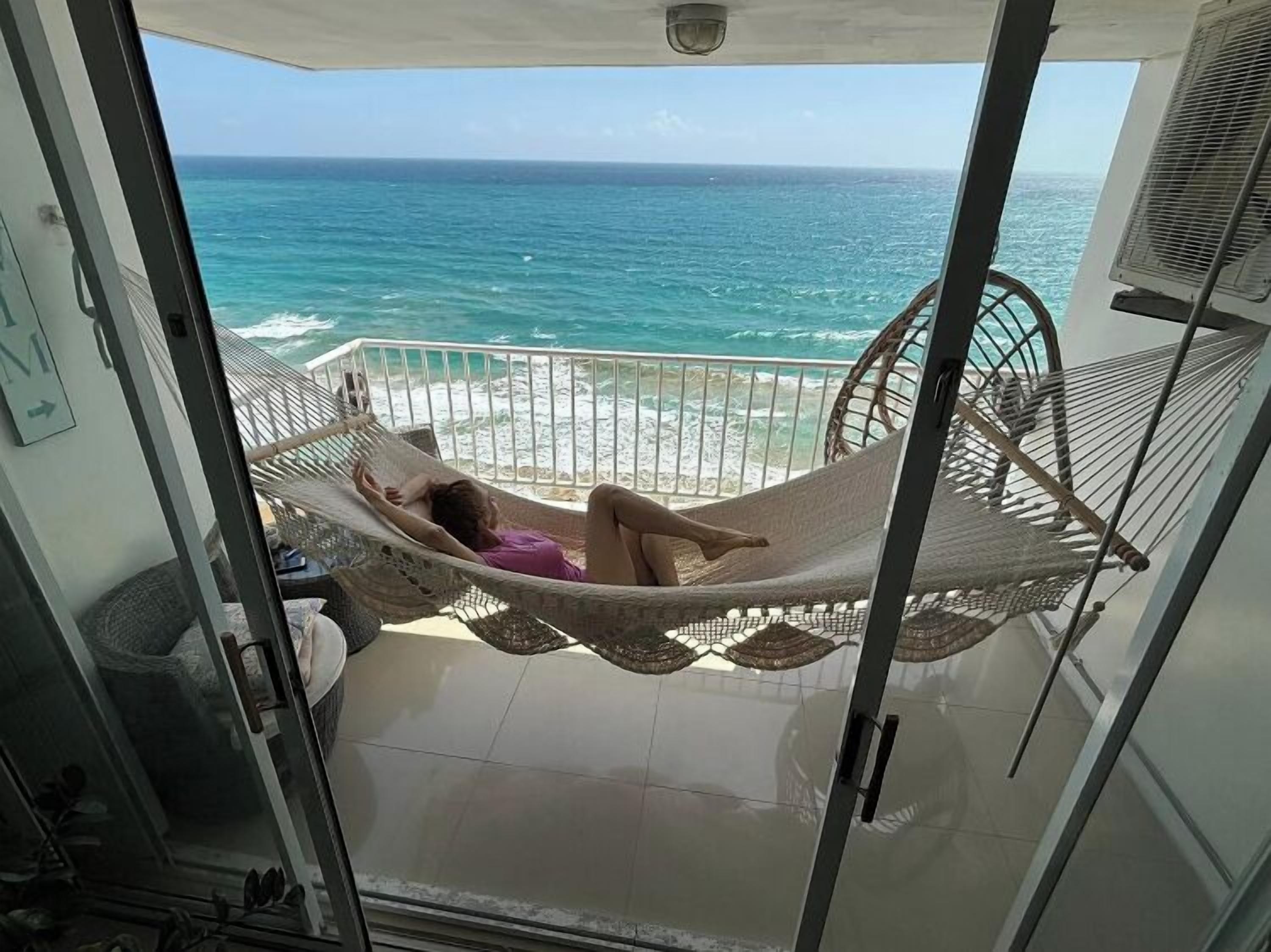 A balcony with a view of the ocean, a hammock, and a fan.