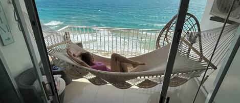 A balcony with a view of the ocean, a hammock, and a fan.