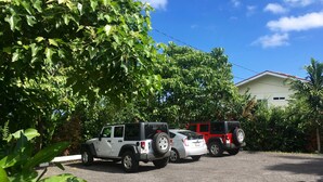 A parking area with two SUVs, surrounded by lush greenery and a building in the background. - Wir sprechen Deutsch. Lovely studio with kitchenette, spacious lanai,TV and WiFi (Kailua Kona)