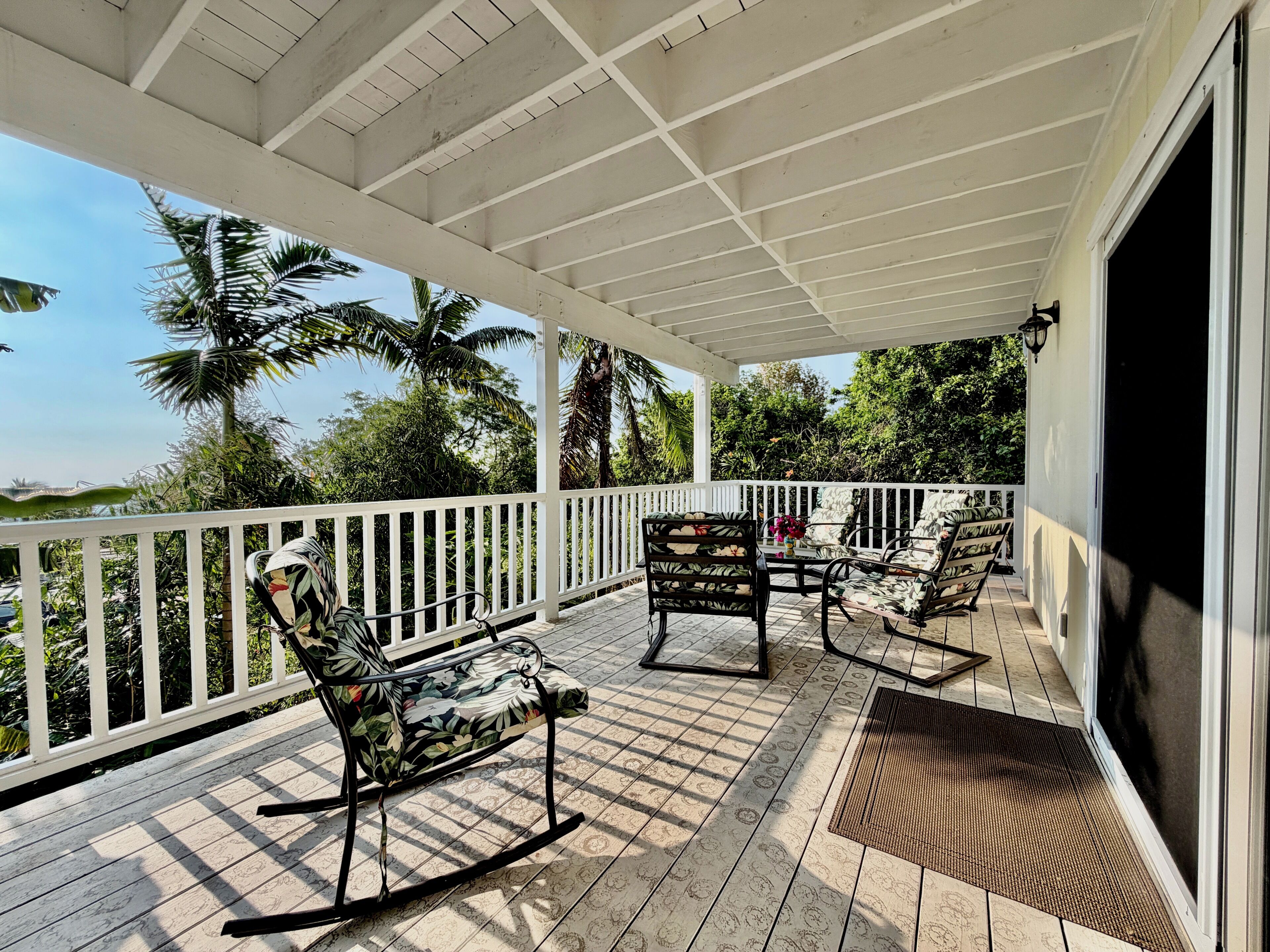 A covered outdoor patio with a white railing, a rocking chair, and a table with chairs.