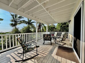 Une terrasse extérieure couverte, dotée d’une balustrade blanche, d’une chaise berçante et d’une table avec des chaises.