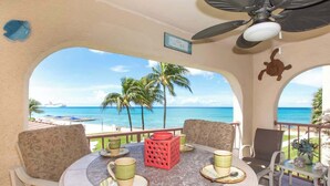 A round table with chairs, a red decorative item, and a view of the ocean and palm trees. - Georgetown Villas #203 Ocean View Condo on 7 Mile (George Town)