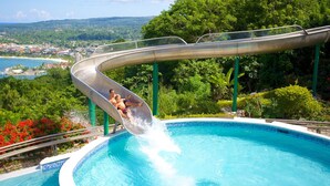 A water slide over a pool with a view of a coastal town. - Villa Serenity · 5BR Fully Staffed Oceanview Villa w/ Chef, Pool & Beach Access (Rio Nuevo bay)
