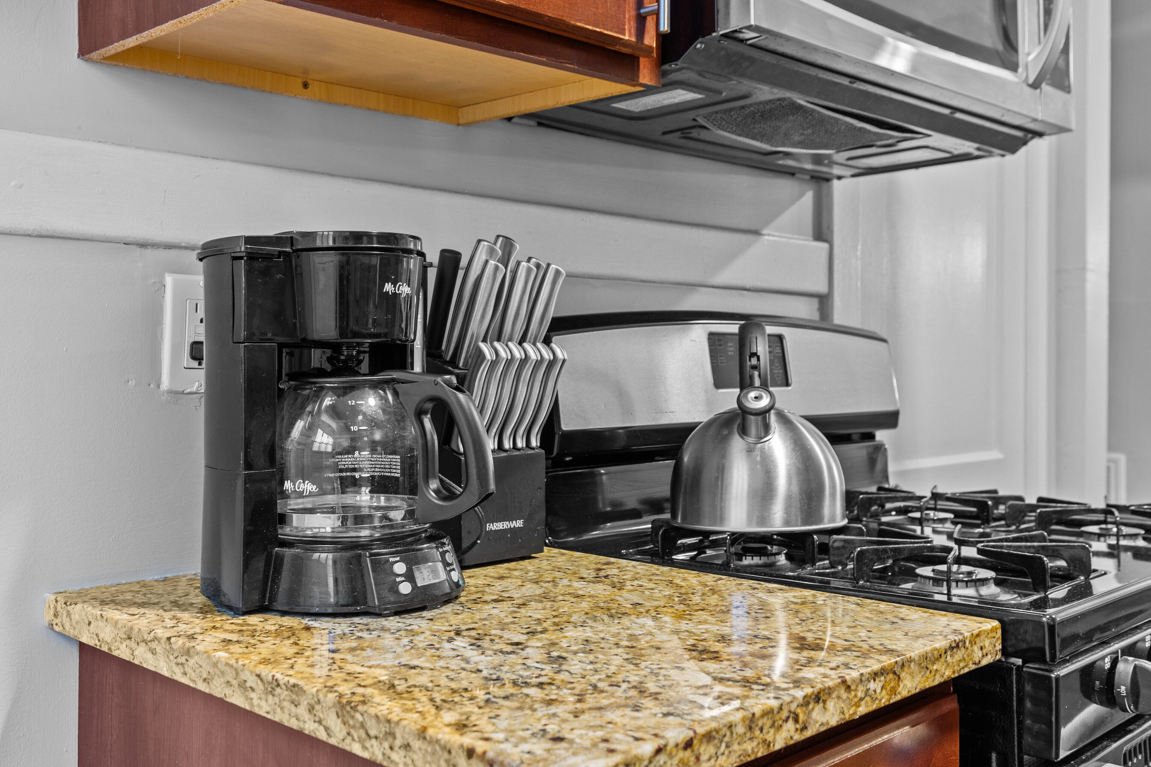 A kitchen with a coffee maker, kettle, and gas stove.