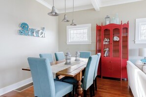 A dining area with a wooden table, blue chairs, pendant lights, a red cabinet, and a window.