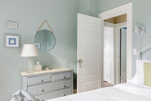 A bedroom with a bed, dresser, mirror, and a door leading to another room.