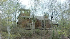 Un edificio rústico de piedra con una chimenea, rodeado de árboles y vegetación exuberante.