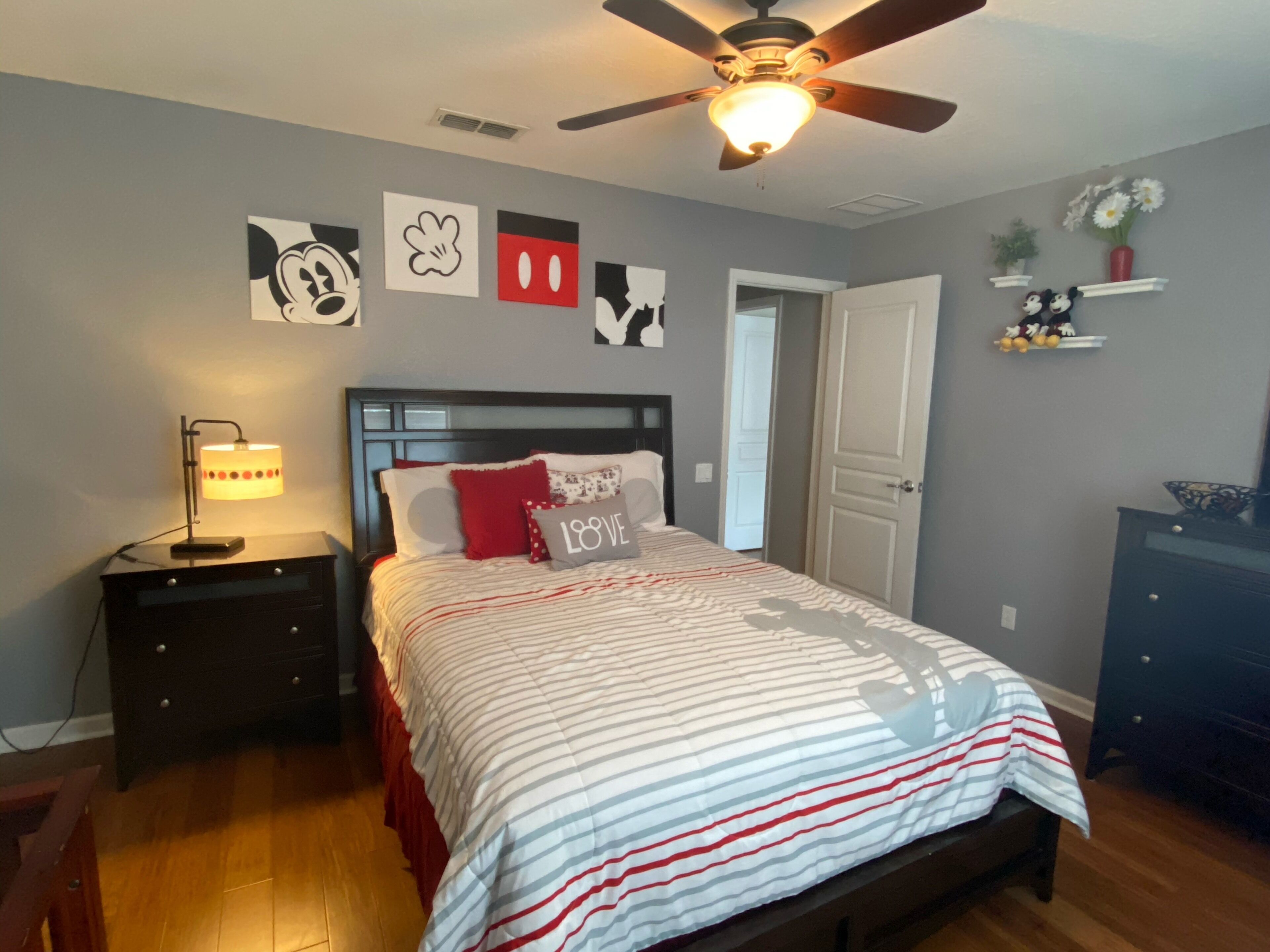 Une chambre à coucher comprenant un lit, des tables de chevet, un ventilateur de plafond et des éléments de décoration murale.