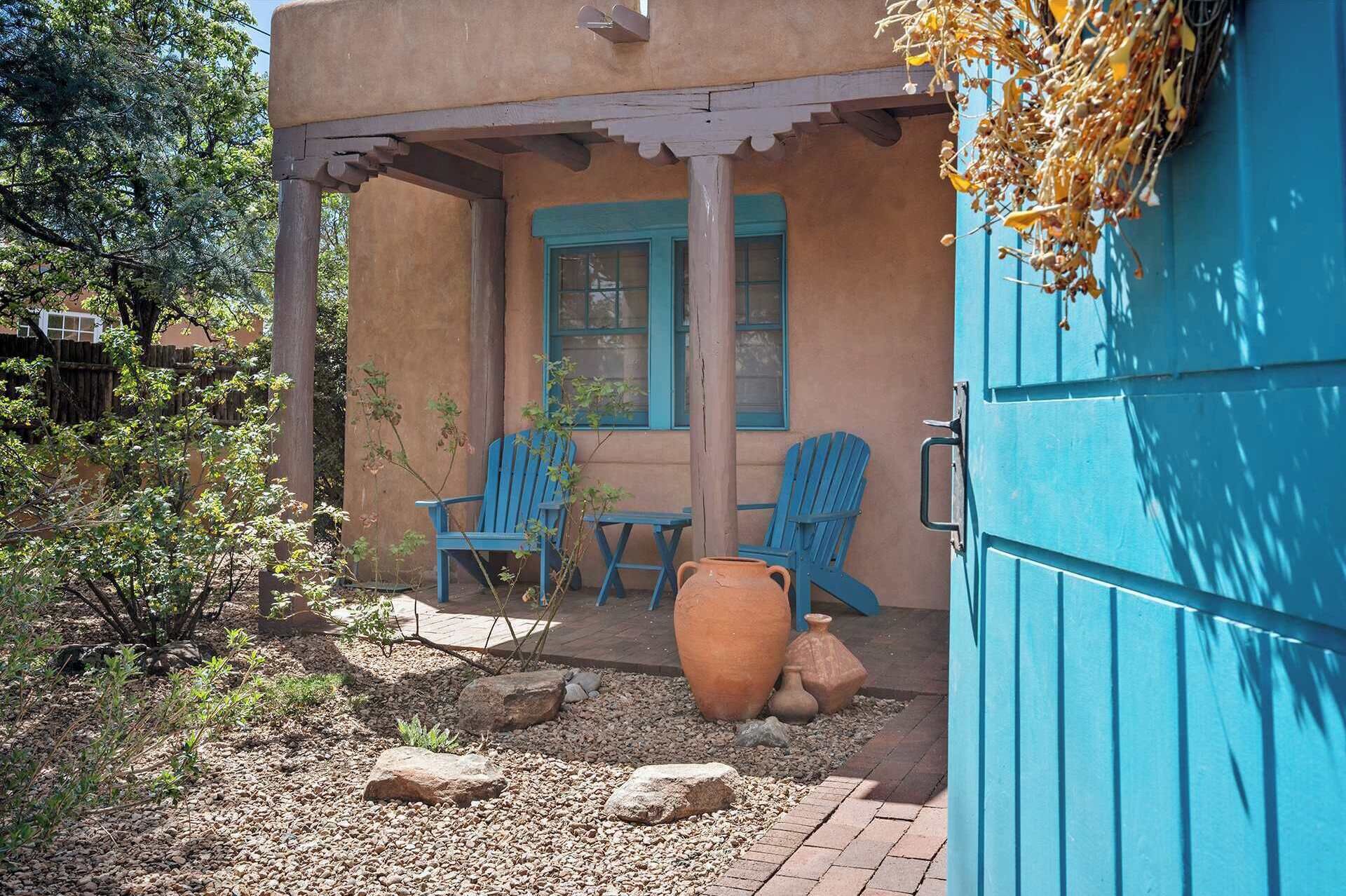 Een rustieke buitenruimte met twee blauwe Adirondack-stoelen en een grote terracotta-pot.