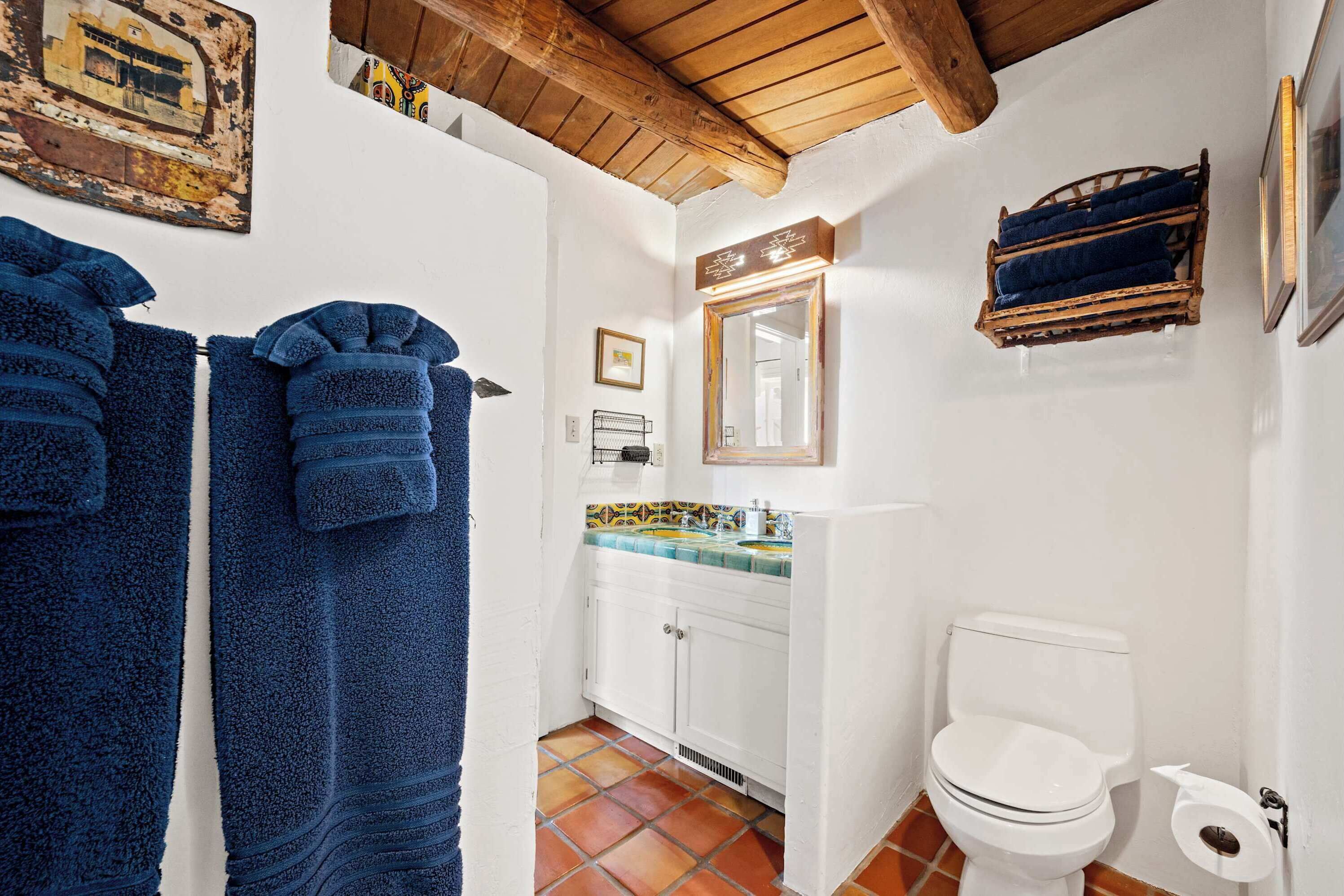 Un baño con inodoro blanco, lavamanos con espejo y toallero con toallas azules.