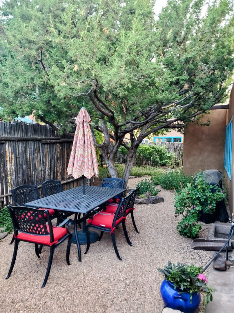 A patio with a table and chairs, surrounded by a wooden fence and a tree.