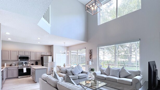 Amplia sala de estar con cocina, ventanas grandes y una lámpara moderna.