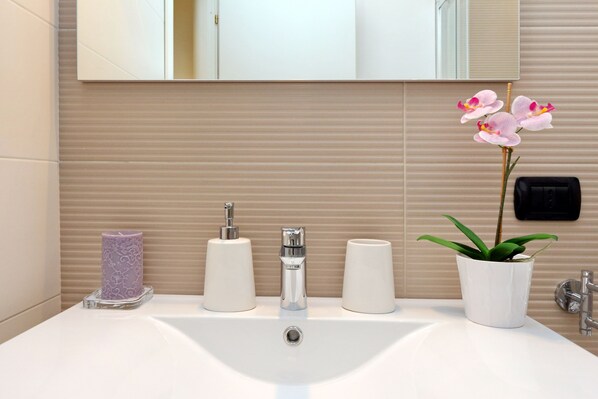 A bathroom sink with a mirror above it, a potted orchid, and three white candles. - The Number 44 - Delightful house in the Vatican area. PRIVATE TERRACE. (Roma)