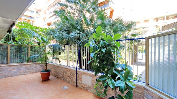 A balcony with potted plants, a tiled floor, and a view of a residential building in the background.