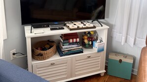A living room with a flat-screen TV on a white entertainment unit, a blue sofa, and a wooden floor. - Lakeview Bungalow with easy walk to Village Fun, Eats, Wine, Craft Beer & Marina (Watkins Glen)
