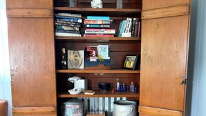 A wooden cabinet with open shelves containing books, jars, and kitchen items. - Lakeview Bungalow with easy walk to Village Fun, Eats, Wine, Craft Beer & Marina (Watkins Glen)