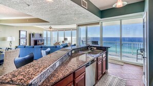 Een ruime keuken met een granieten aanrecht en een groot eiland, een eethoek met blauwe meubels, en een balkon met uitzicht op de oceaan.