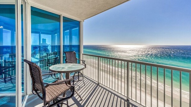 Een balkon met uitzicht op de oceaan en een glazen deur naar een binnenruimte met tafels en stoelen.
