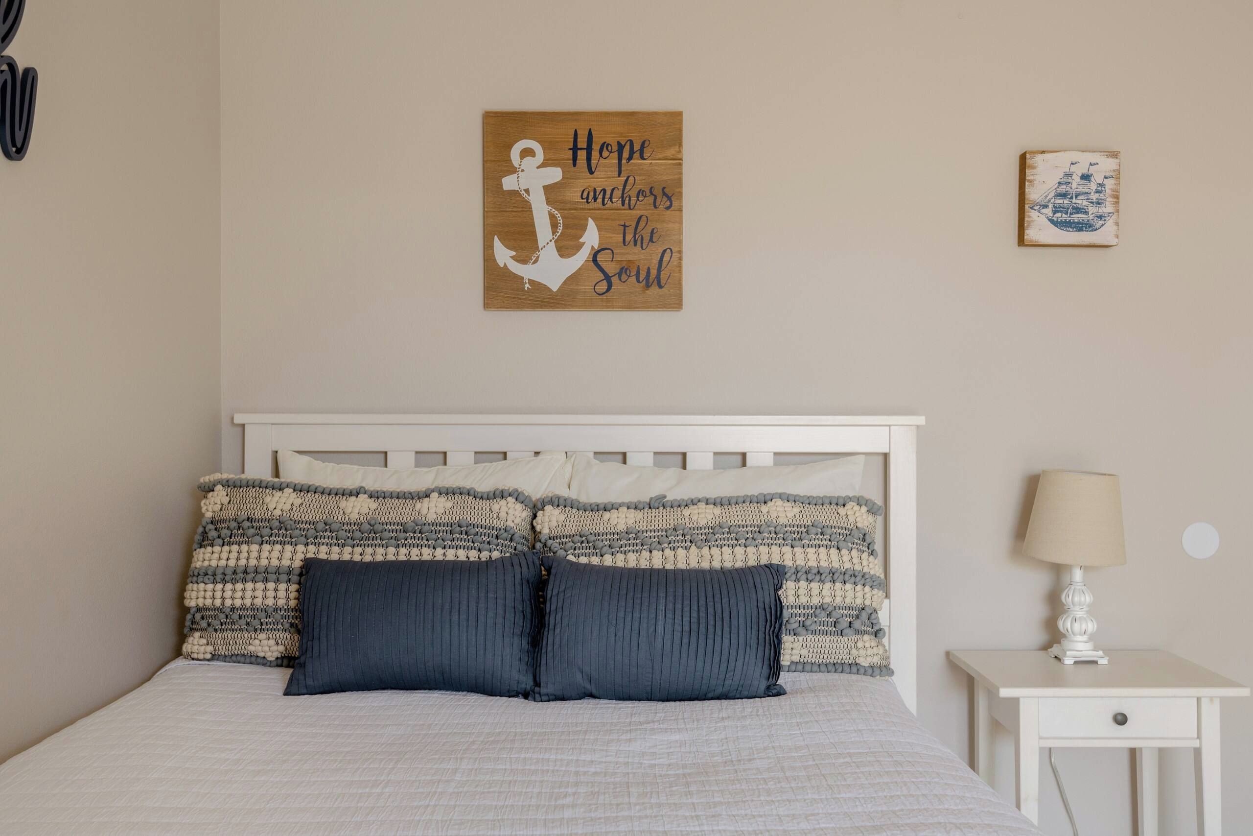 Een slaapkamer met een bed, kussens, een nachtkastje, een lamp en wanddecoratie.