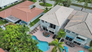 Une maison à deux étages avec une piscine, un patio doté de mobilier d’extérieur et un jardin bien entretenu.