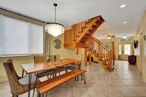 A dining area with a wooden table and chairs, a chandelier, and a staircase leading to another level.
