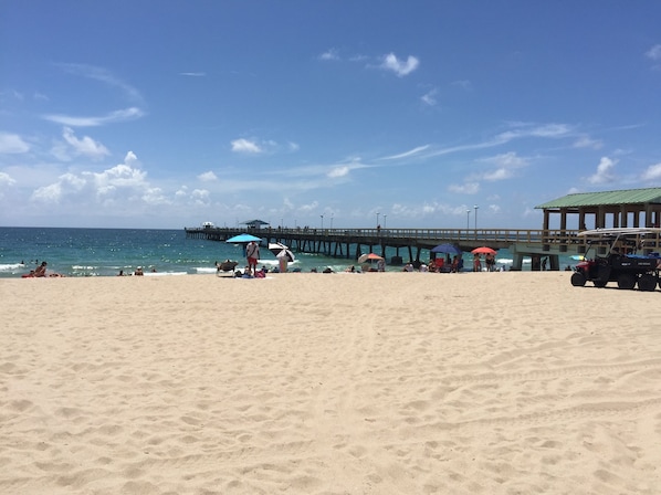 Una playa con un muelle que se adentra en el océano, con sombrillas y sillas de playa.