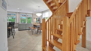 Un intérieur moderne avec un escalier en bois, un coin repas comprenant des chaises et une table, et de grandes fenêtres offrant une vue sur la verdure.