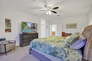 Un dormitorio con cama, cómoda, silla, ventilador de techo y obras de arte en las paredes.