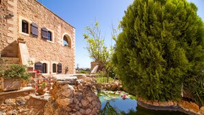 A stone building with arched windows and a small pond with lily pads. - Purple villa Malotira - 1 bedroom -veranda -roof terrace - mountain and sea view (Chania)