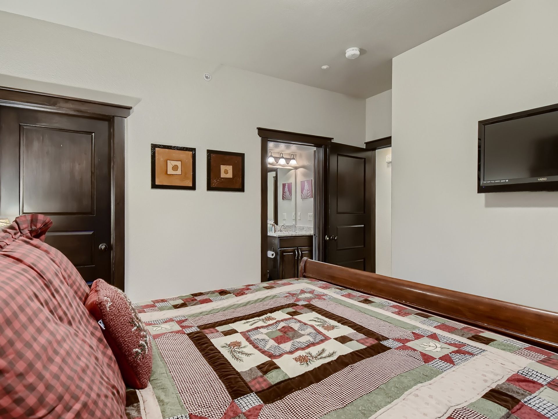 A bedroom with a large bed, a TV mounted on the wall, and two framed pictures on the wall.